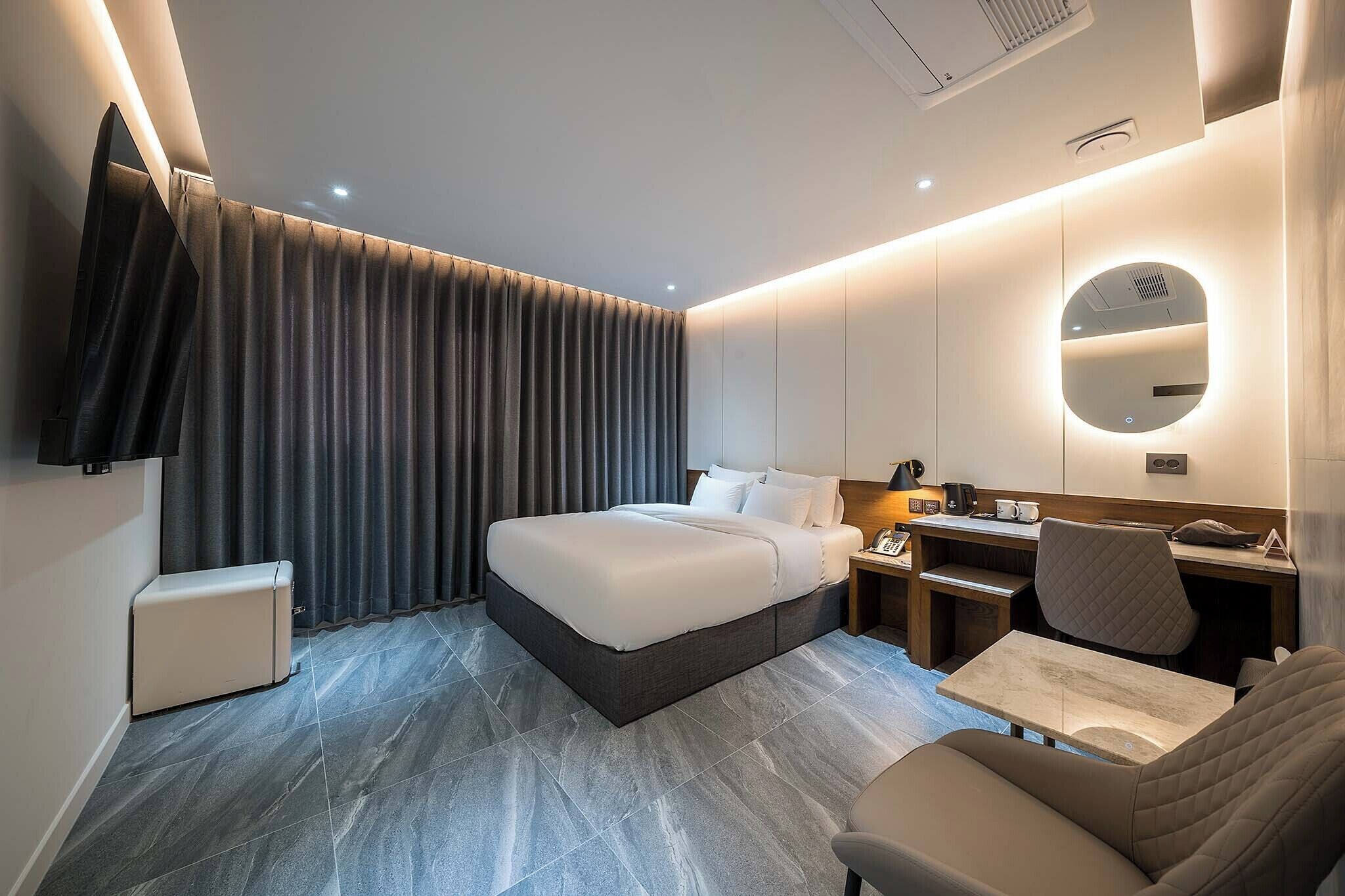 A modern hotel room with a bed, desk, chair, and a small table.