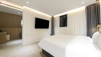 Una habitación de hotel moderna con una cama grande, un televisor de pantalla plana montado en la pared, un escritorio con una silla y un armario.