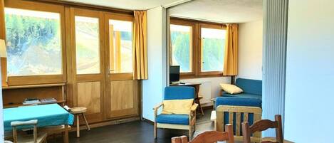 A room with a wooden table, chairs, a sofa, and a TV.