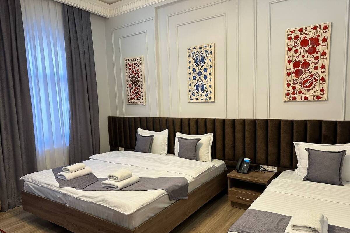 Una habitación de hotel con una cama grande, una cama más pequeña, una mesita de noche con un teléfono y una mesita con una lámpara.