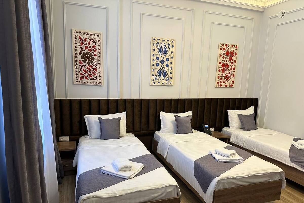 Habitación de hotel con tres camas individuales, cada una con una almohada y una toalla doblada. La habitación tiene un cabecero de madera, piso de madera y tres adornos de pared.