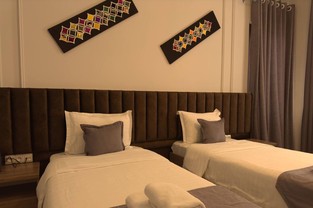 Habitación de hotel con dos camas, cada una con cabecera, almohadas y toallas dobladas con cuidado.