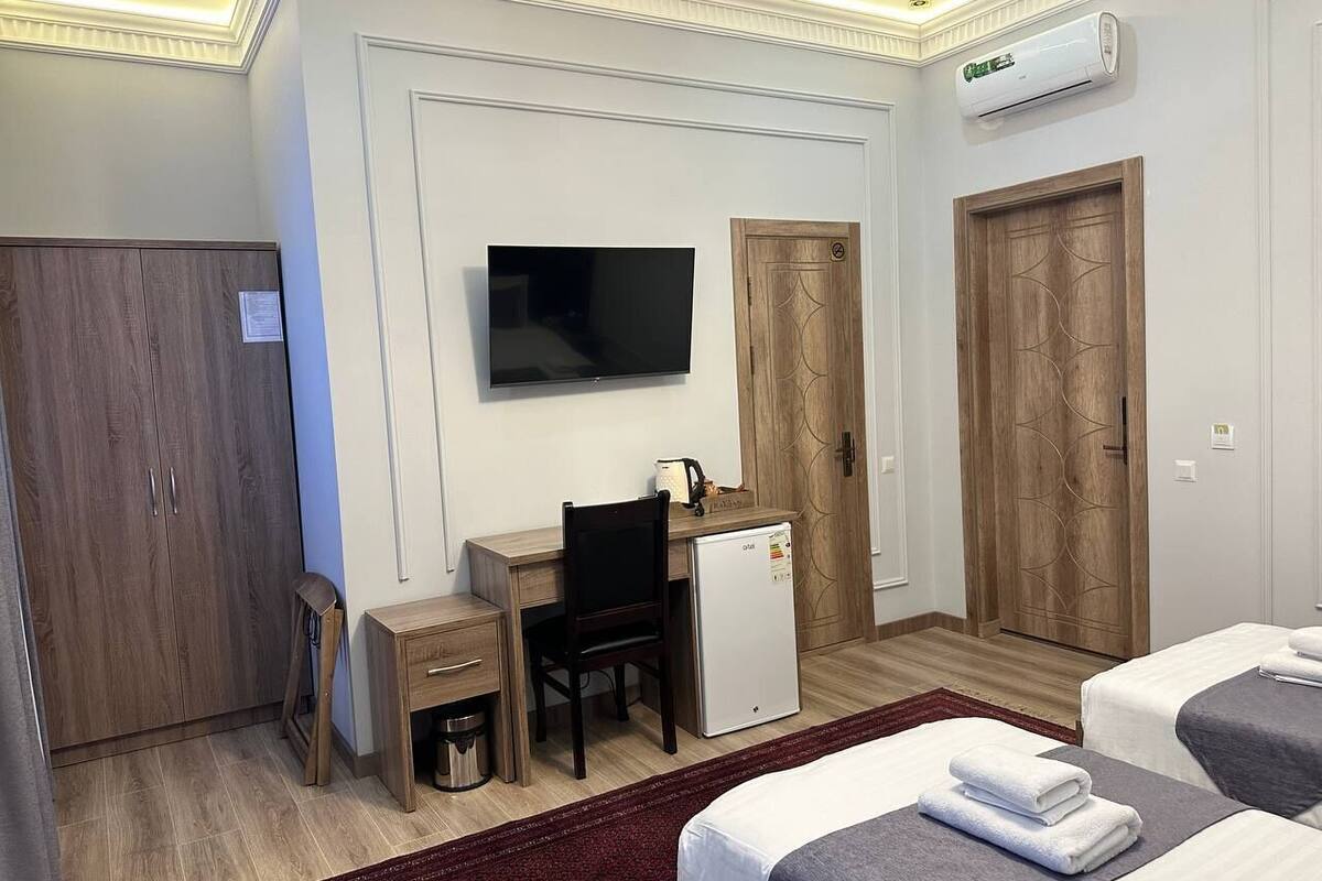 Habitación de hotel con escritorio, televisión, refrigerador pequeño, dos camas y armario.