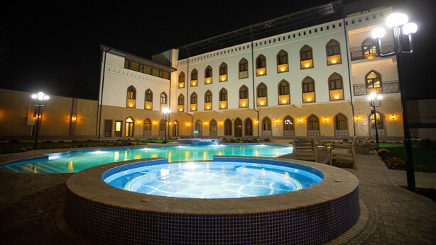 A large building with multiple arched windows and a swimming pool area with a hot tub. - Rayyan Hotel Samarkand (Samarkand)