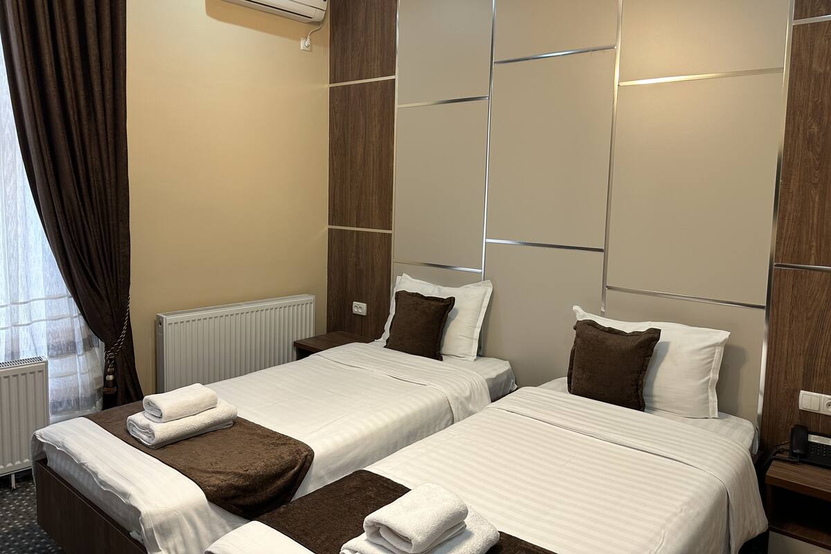 Habitación de hotel con dos camas, un radiador, un equipo de aire acondicionado, un teléfono y una ventana con cortinas.