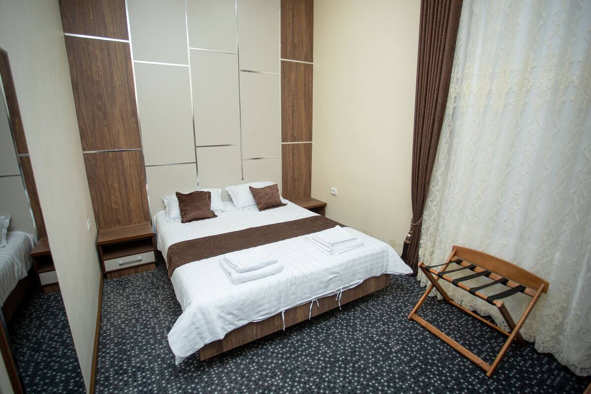 Un dormitorio con cama, un banco de madera y una ventana con cortinas.