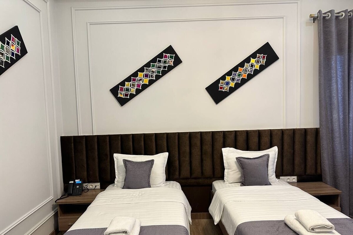 A hotel room with two beds, a dark headboard, white walls, and a curtain.