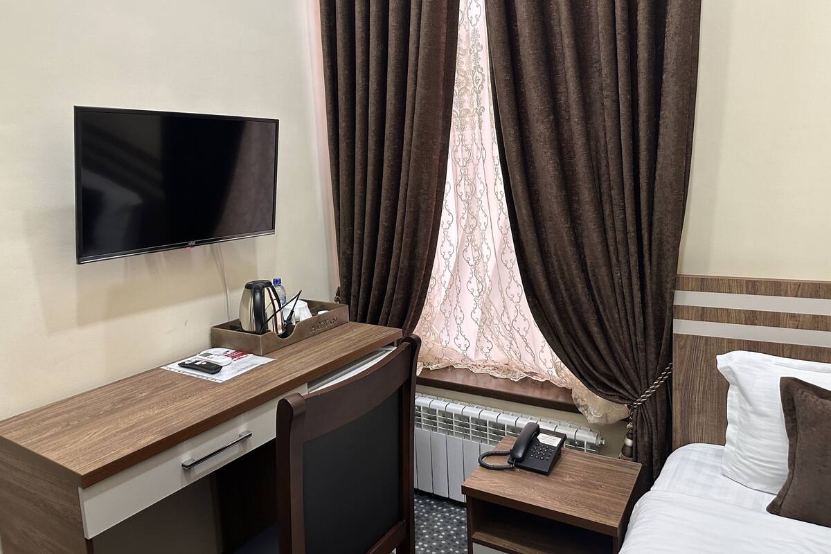 Habitación de hotel con televisión de pantalla plana, escritorio de madera con cafetera, teléfono y cama con ropa blanca.