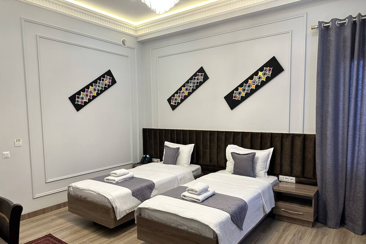 Habitación de hotel con dos camas, cabecera oscura y alfombra roja.
