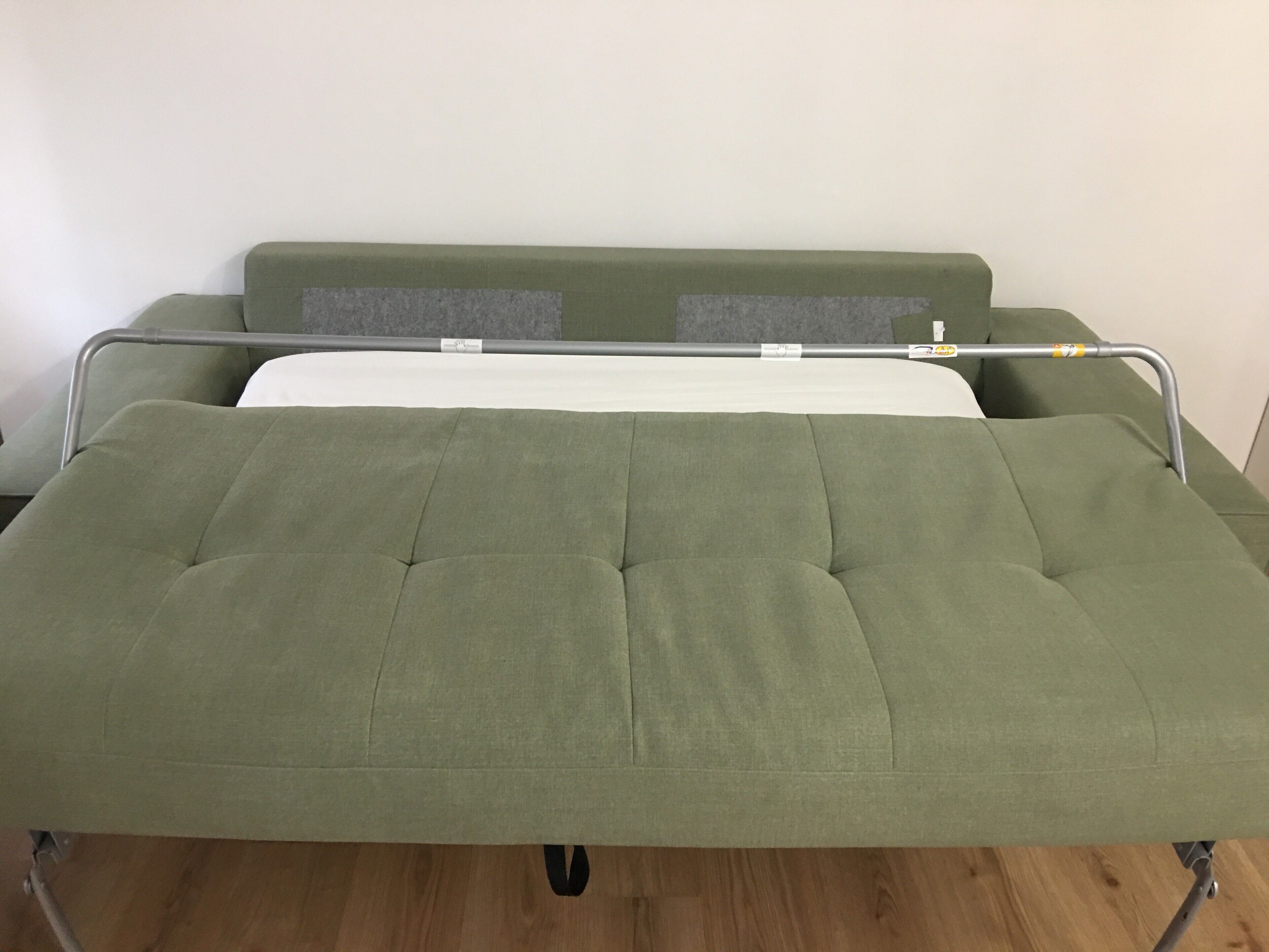 A green sofa bed with a metal frame, a white mattress, and a grey cushion.