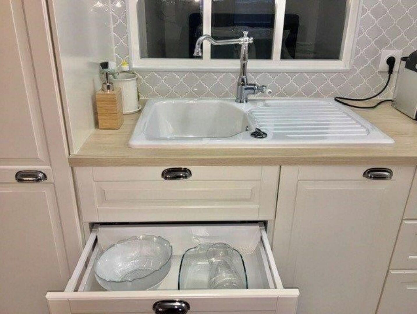A kitchen with a sink, countertop, and a drawer with plastic containers.