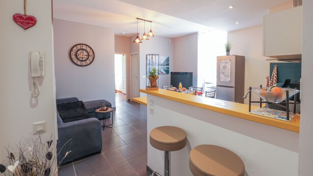 Une cuisine moderne avec un coin bar, un canapé gris et une horloge murale.