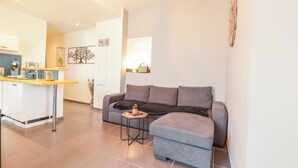 Un salon moderne avec un canapé gris, une petite table d’appoint et un coin cuisine doté d’un comptoir-bar.