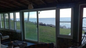 A cozy room with a large sliding glass door leading to a grassy area with a view of the sea. There are two chairs and a small table in the room.