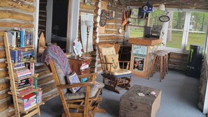 A cozy log cabin interior with a bookshelf, rocking chair, and a sign indicating a 'Beef Tender' menu.