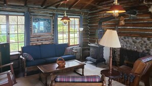 A log cabin interior with a blue sofa, wooden furniture, a stone fireplace, and a large window.