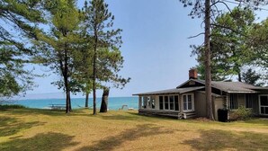 A cabin with a large window overlooking a body of water, surrounded by trees.