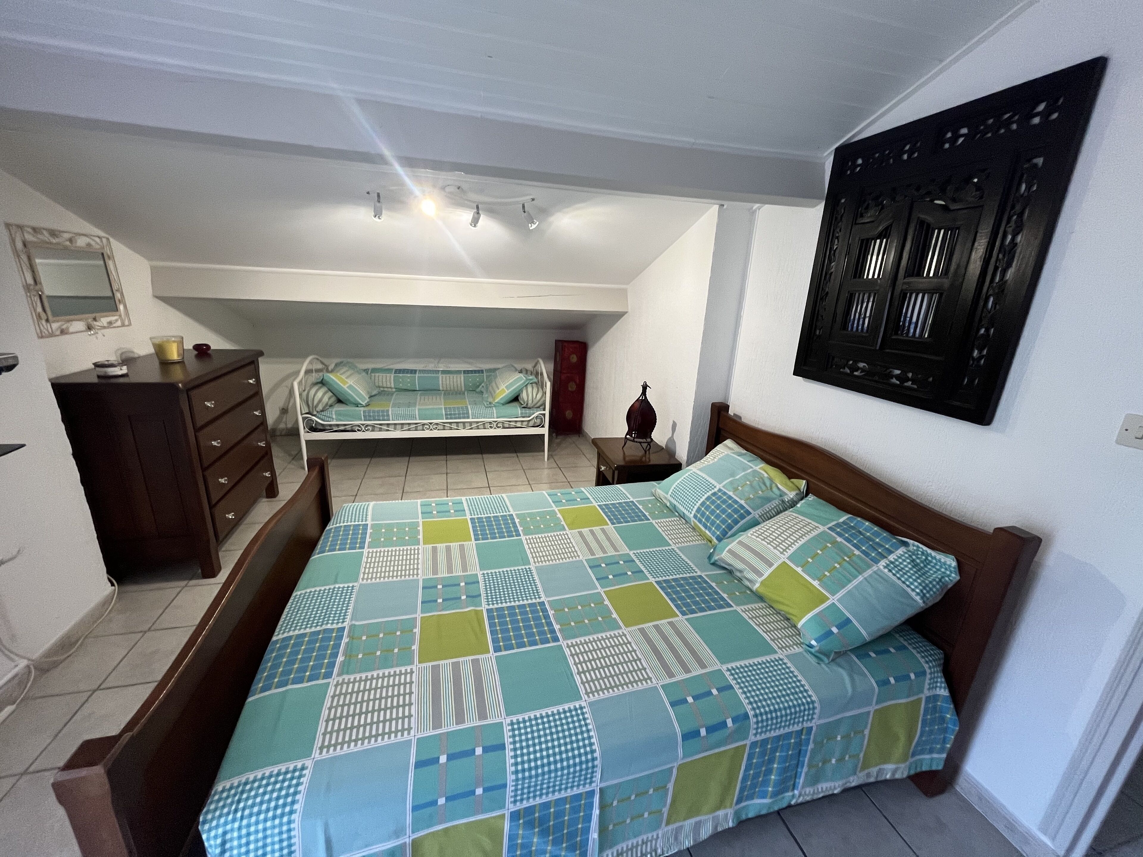 A bedroom with a large bed, a dresser, a nightstand, and a wall-mounted artwork.