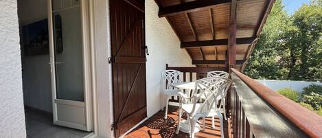 Une terrasse en bois dotée d’un espace couvert, d’une porte-fenêtre coulissante et de chaises d’extérieur blanches.