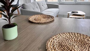 Un salon moderne avec un canapé gris, une table à manger en bois agrémentée de sets de table en fibres naturelles et une plante en pot.