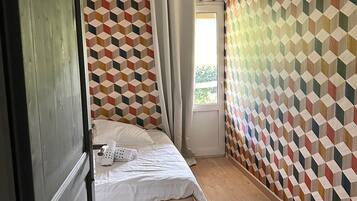 A bedroom with a geometric-patterned wall, a bed with white bedding, a hanging light fixture, and a window with curtains.