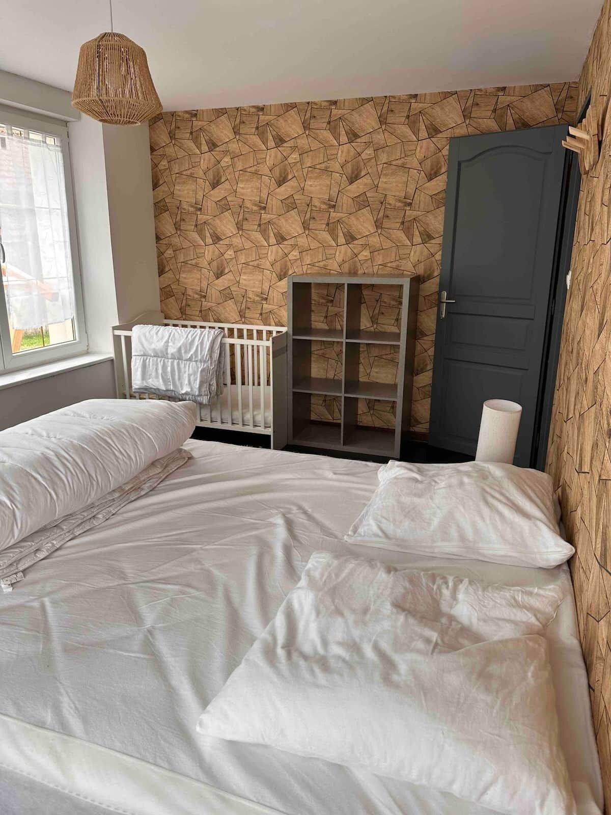 Une chambre à coucher avec un grand lit, un berceau, une armoire et un mur orné d’un motif géométrique.