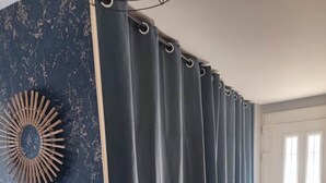 Une pièce avec un mur bleu foncé à la texture particulière, une grande fenêtre avec des rideaux et une porte blanche.