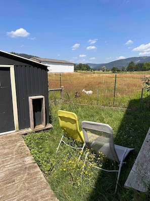 Et landligt udendørsområde med en træterrasse, en gul stol og en metalstol.