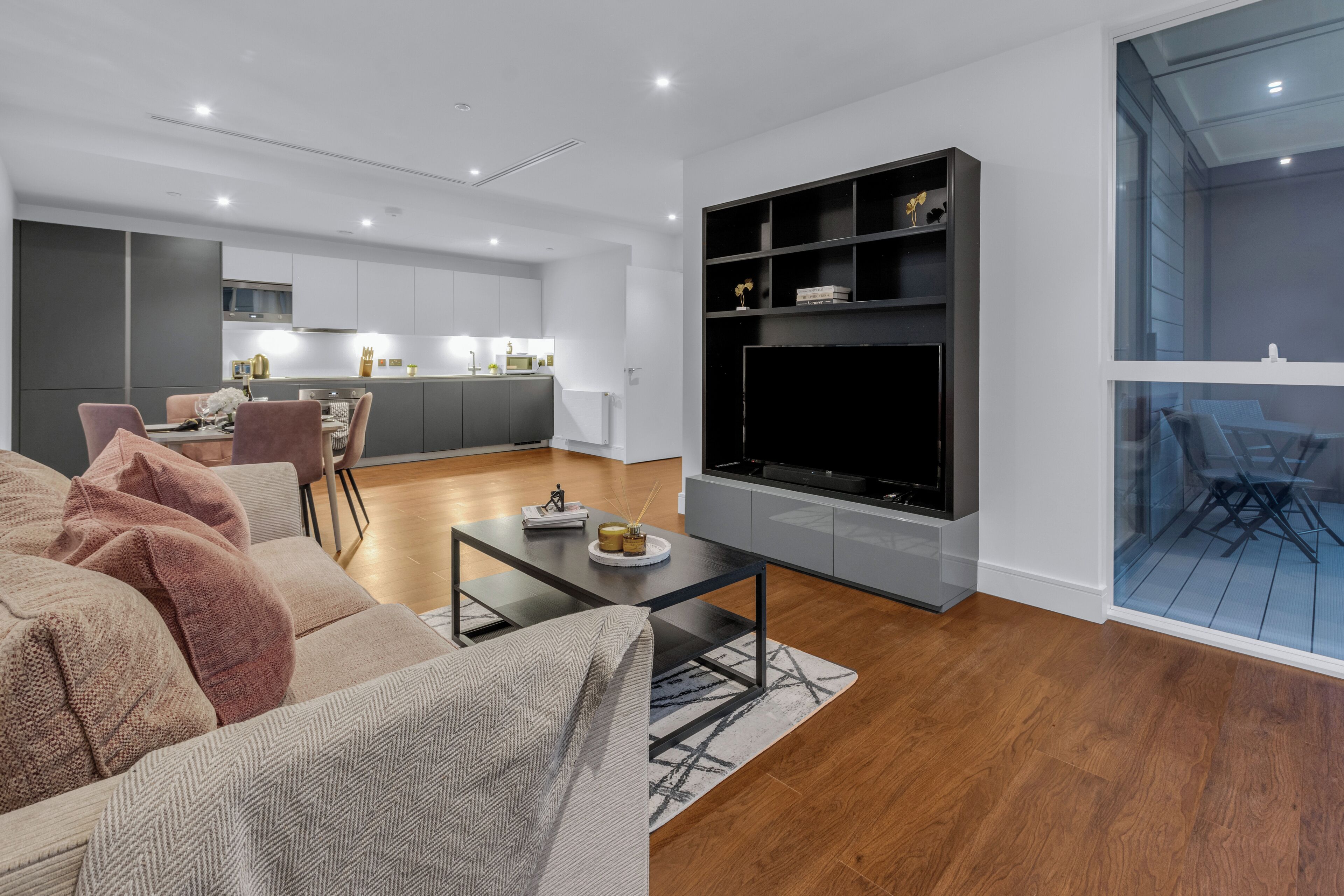 A modern living room with a sofa, coffee table, and TV. There is a kitchen in the background with a dining area.