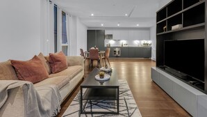 Een moderne woonkamer met een bank, salontafel en televisie. Achtergrond toont een keuken met een eethoek.
