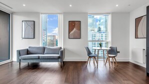 Een moderne woonkamer met een grijze bank, een eettafel met stoelen en grote ramen met uitzicht op de stad.