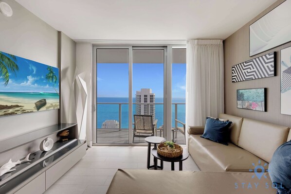 Un salon moderne avec balcon, une grande peinture représentant une plage et une vue sur l’océan.