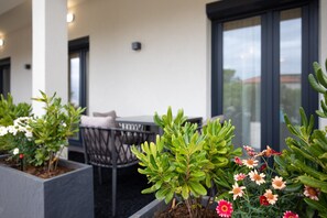 A modern outdoor seating area with a table and chairs, surrounded by potted plants and flowers.