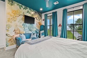 A bedroom with a large bed, a TV mounted on the wall, and a view of the outdoors through a window. - River View Luxury with Heated Pool & Take Ferry to French Quarter (New Orleans)