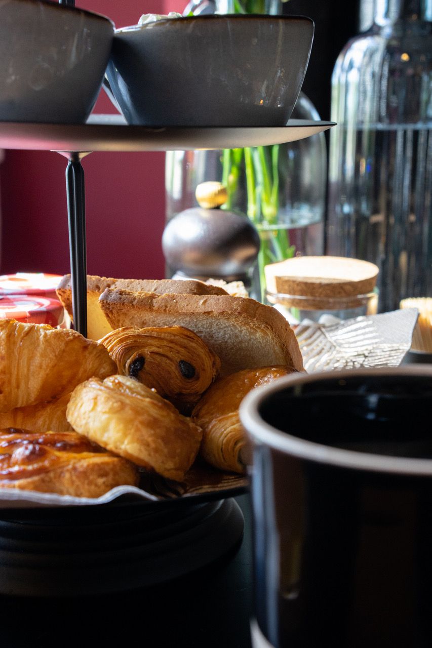 Variedad de pasteles y panes en una bandeja, con una taza de café al frente.