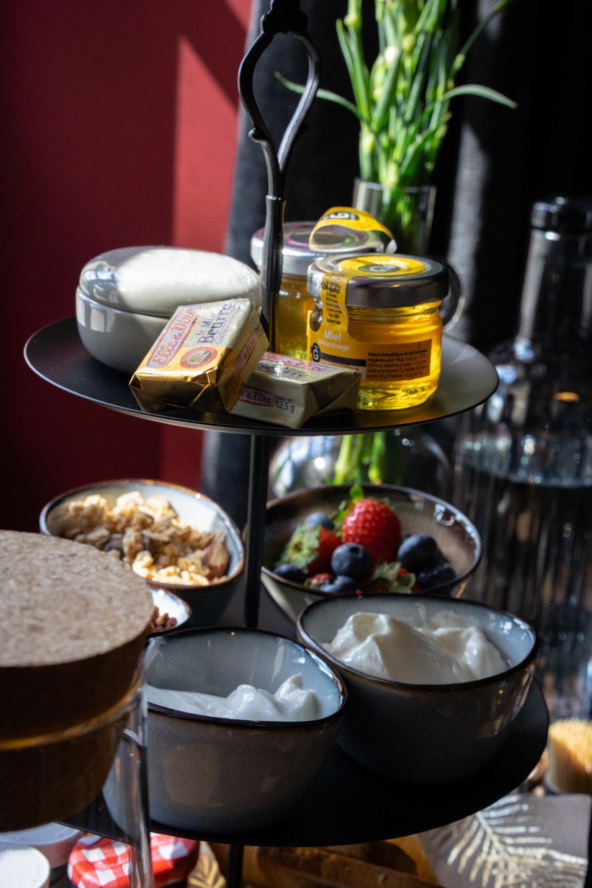 Un plateau de service à trois niveaux, sur lequel sont disposés divers aliments, notamment du fromage, du miel et des fruits, et qui est placé sur une table.