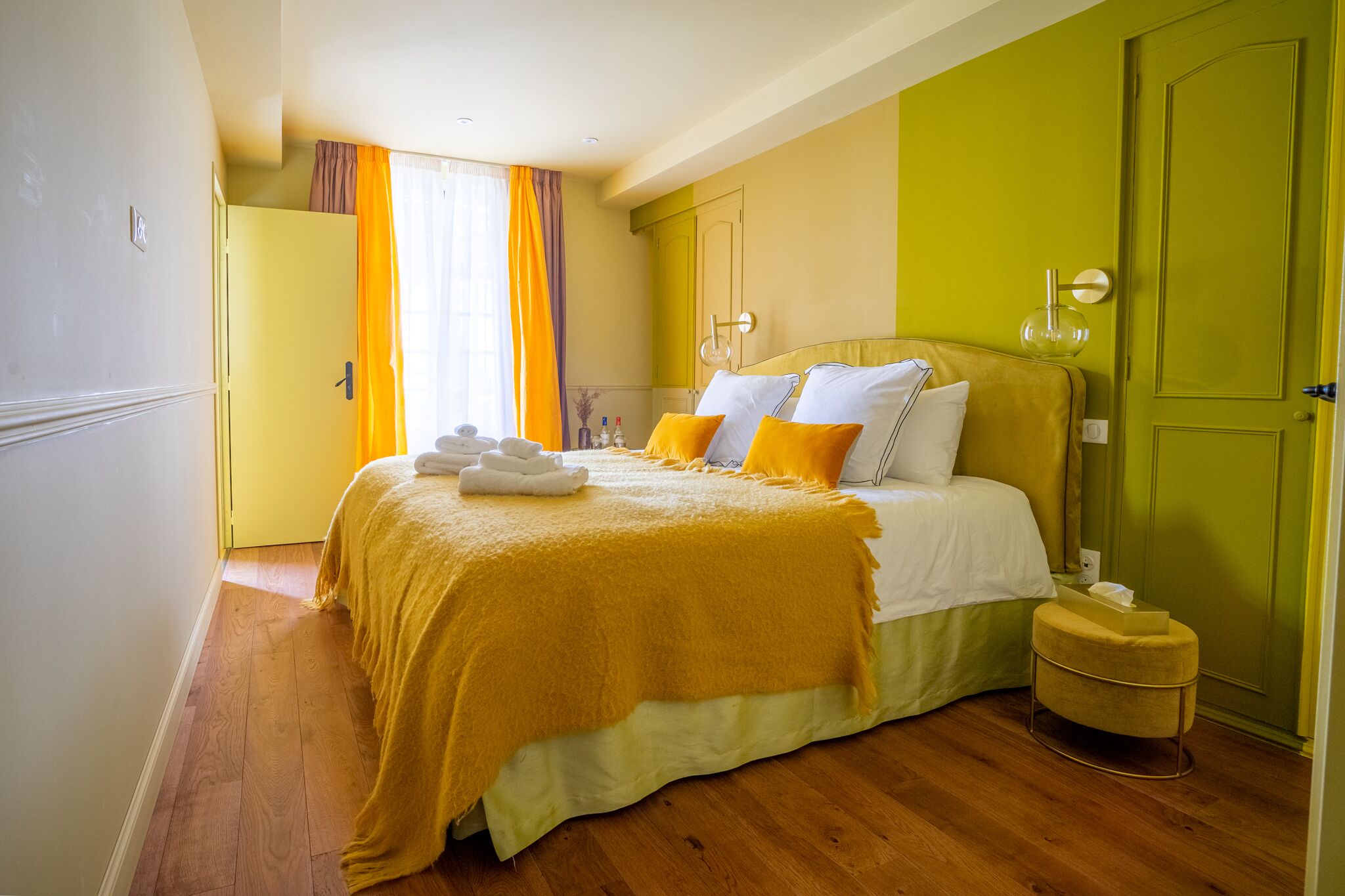 Una habitación de hotel con una cama, un armario amarillo, una puerta verde y un taburete pequeño.