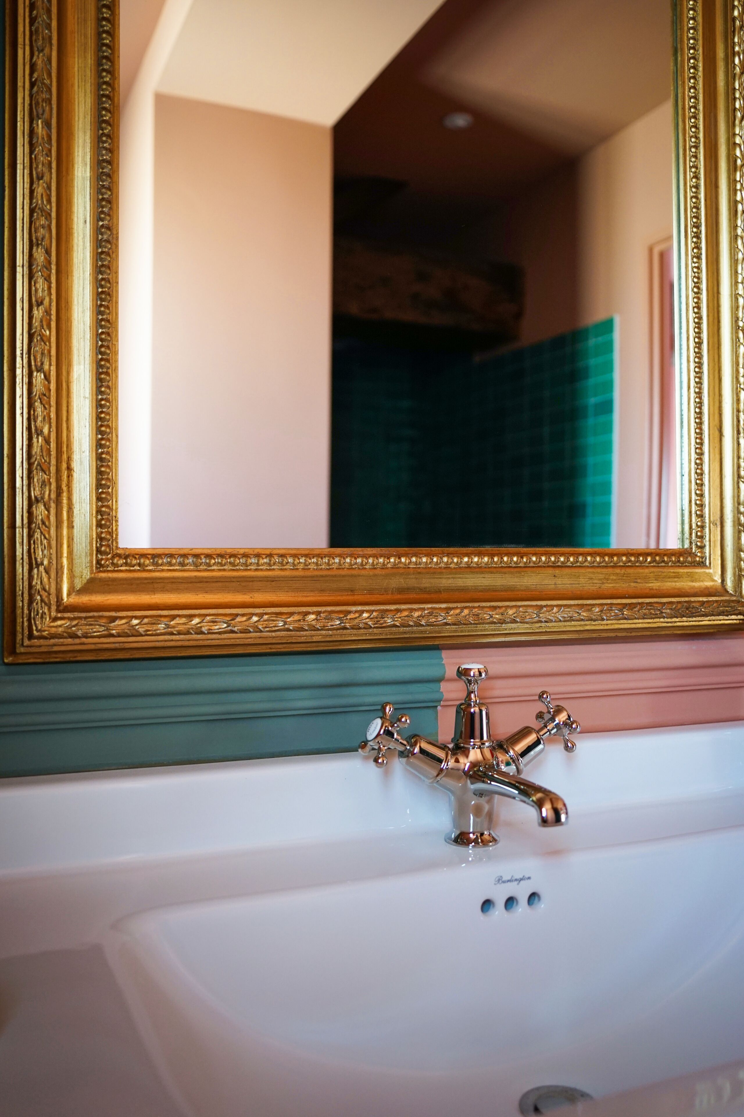 Un baño con un espejo con marco dorado, un lavabo blanco y una pared con azulejos verdes.