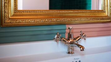 Un baño con un espejo con marco dorado, un lavabo blanco y una pared con azulejos verdes.
