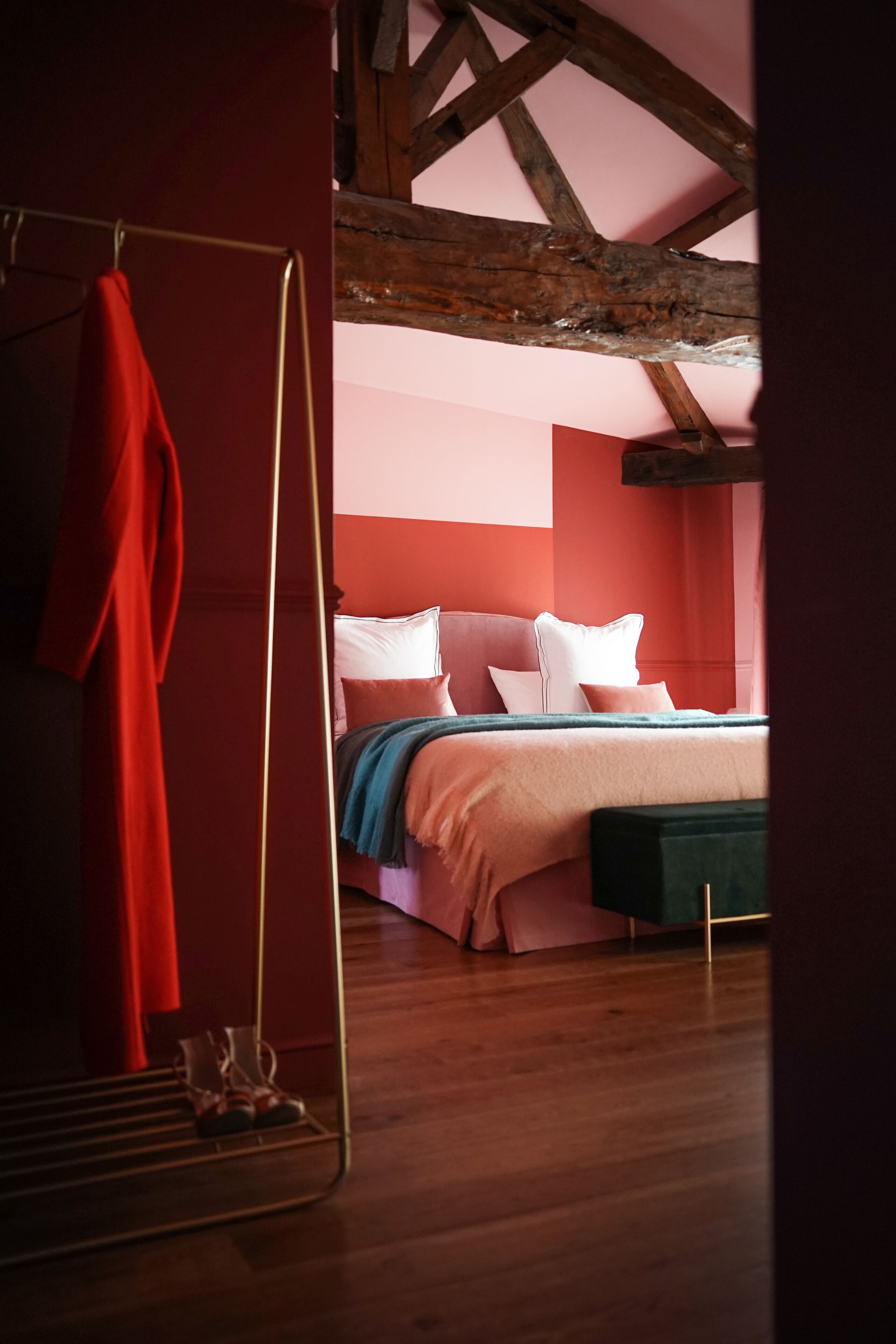 A bedroom with a bed, pillows, a bench, and a red robe hanging on a rack.