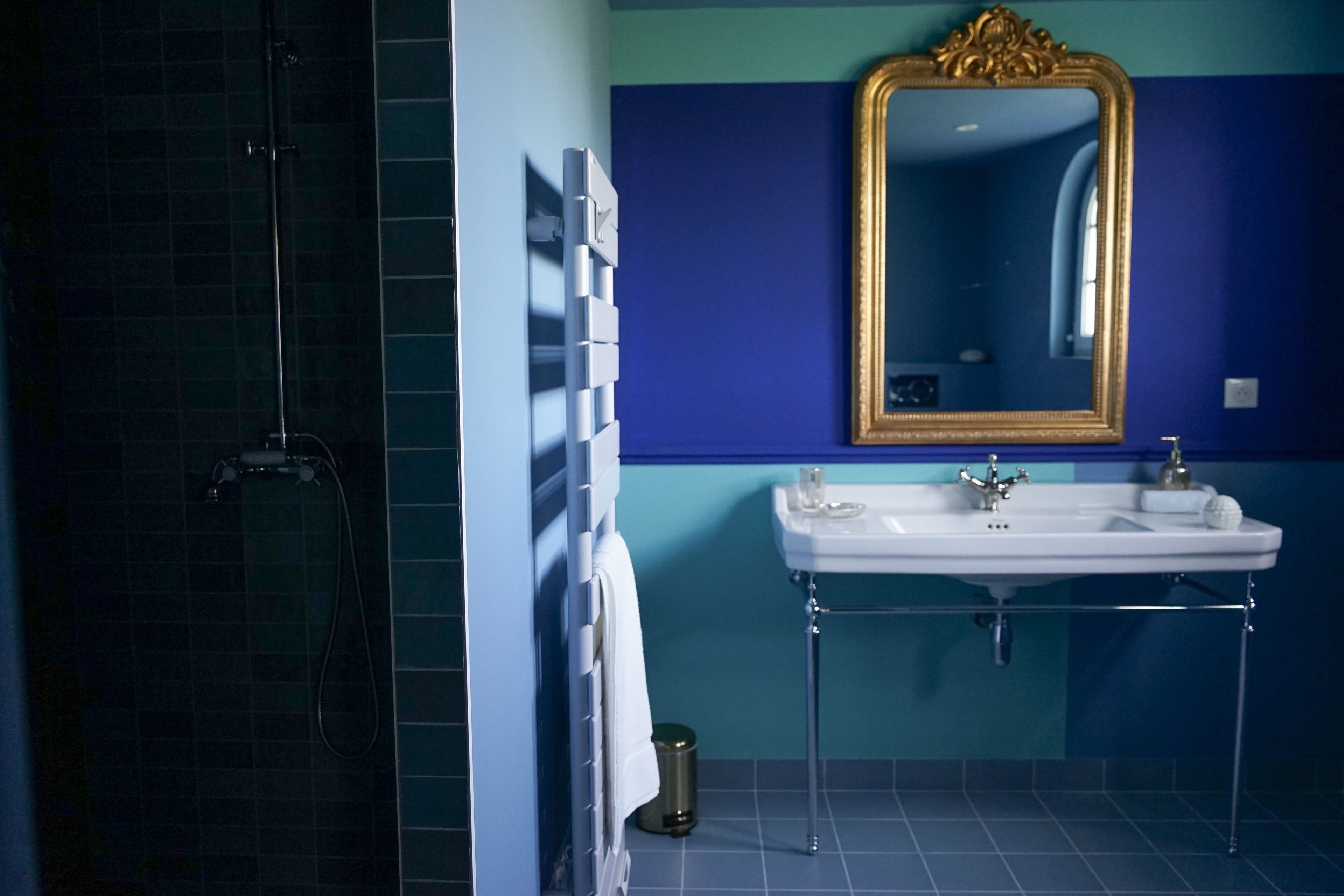 Un baño con cabina de ducha de vidrio, un lavabo blanco con detalles cromados y un espejo grande con marco dorado.