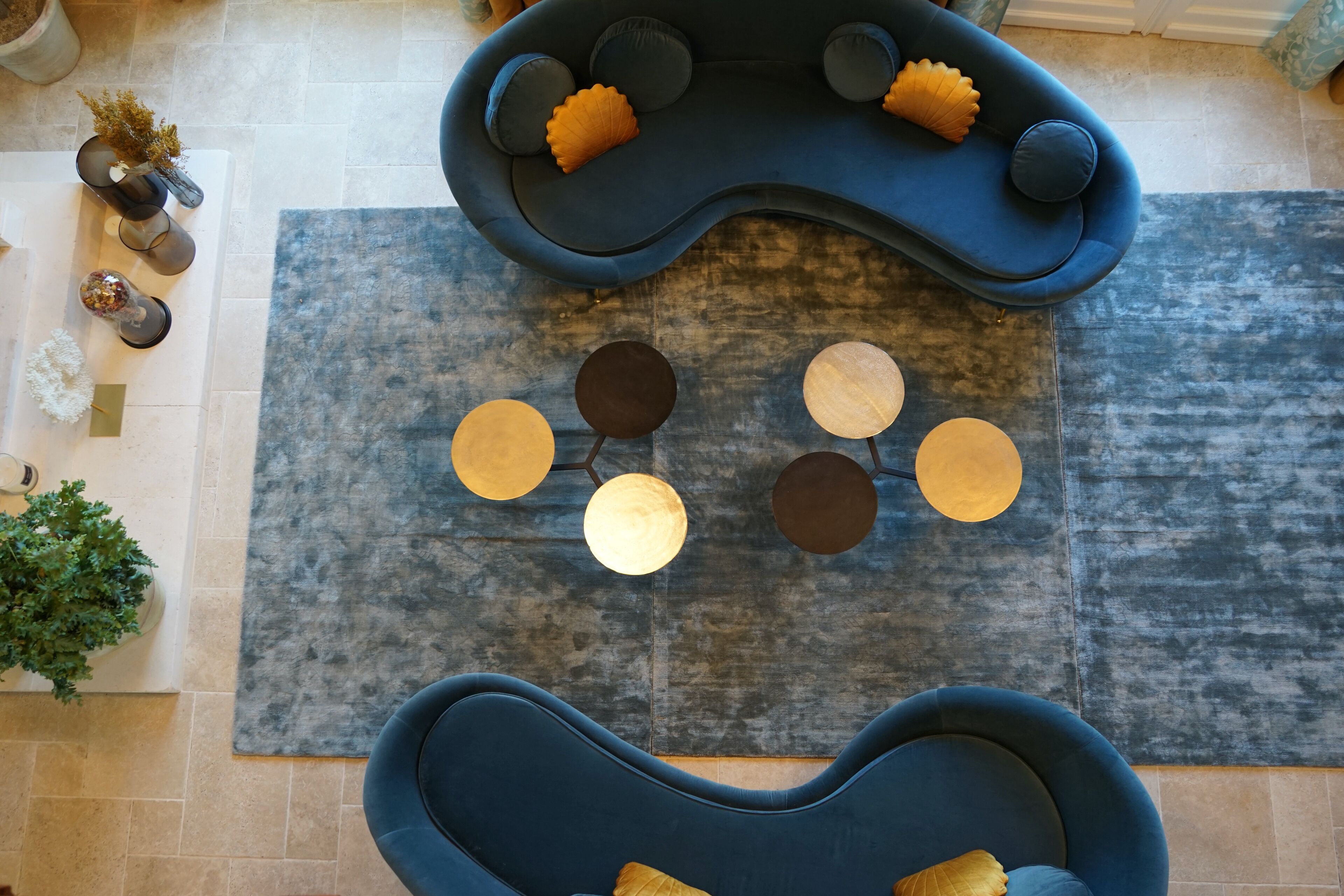 A modern living room with two blue sofas, a grey rug, and decorative round tables.