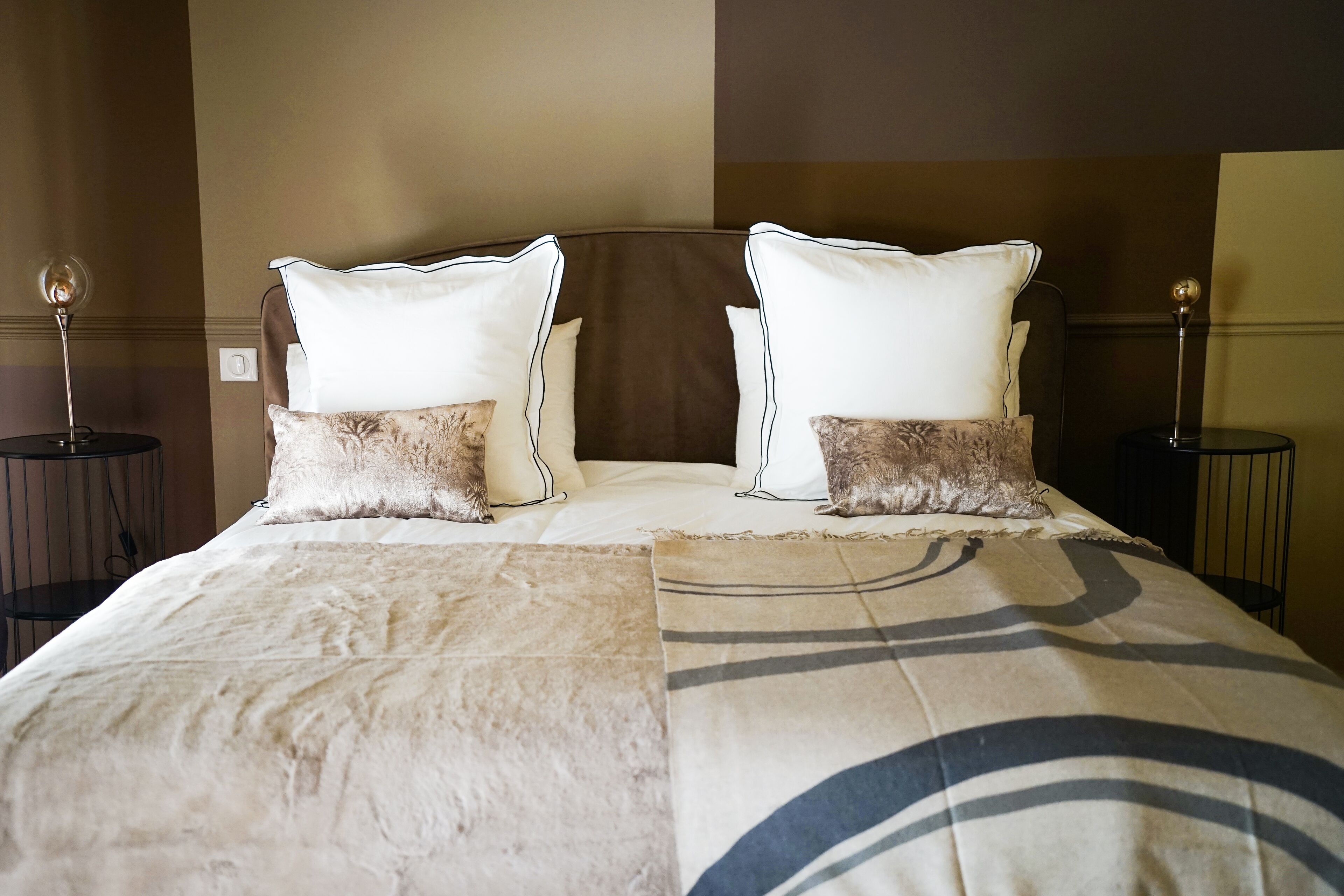 Una cama bien hecha con un edredón estampado, dos almohadas y dos mesitas de noche con lámparas.