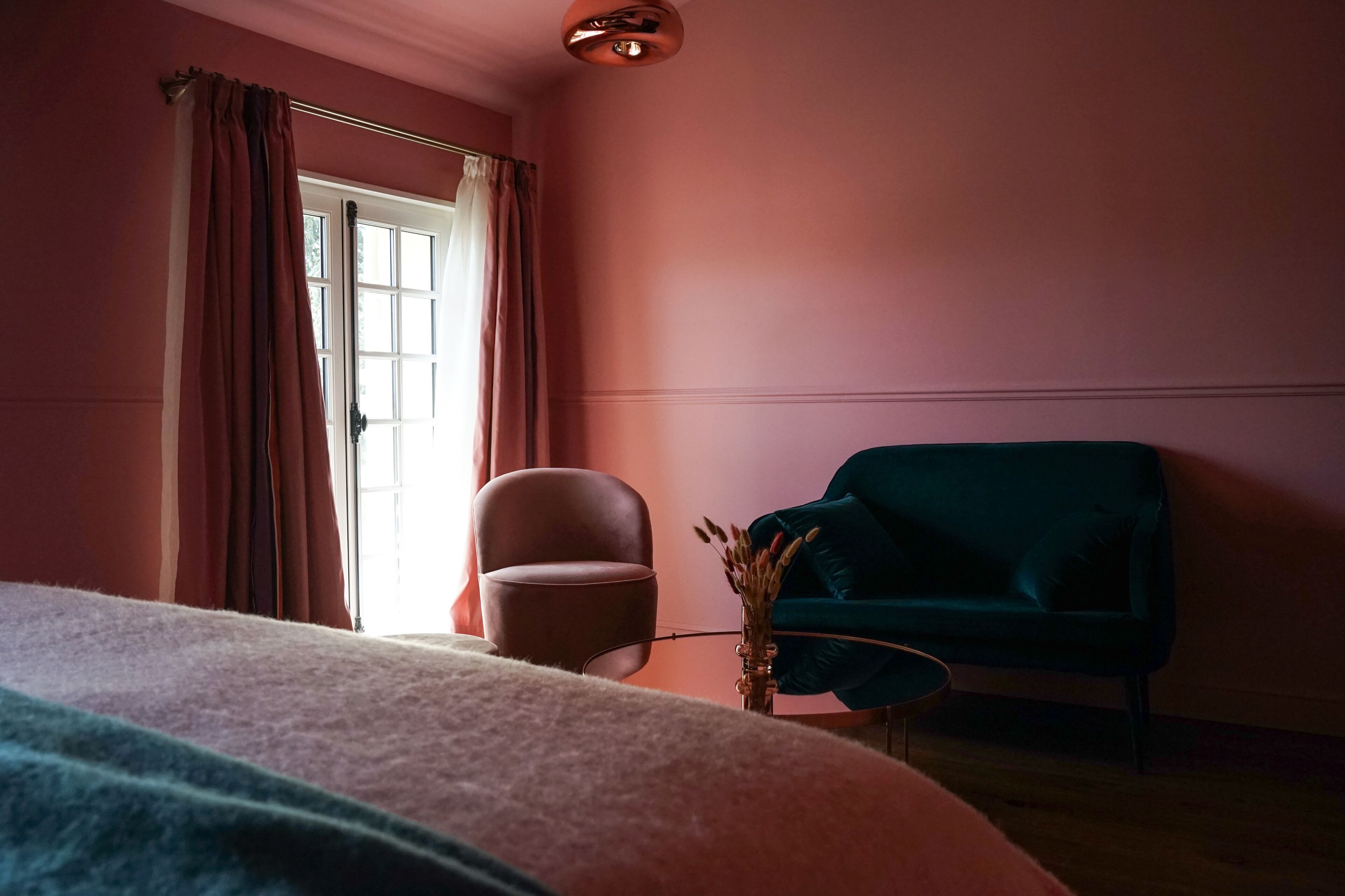 A room with a bed, a chair, a small table, and a window with curtains.