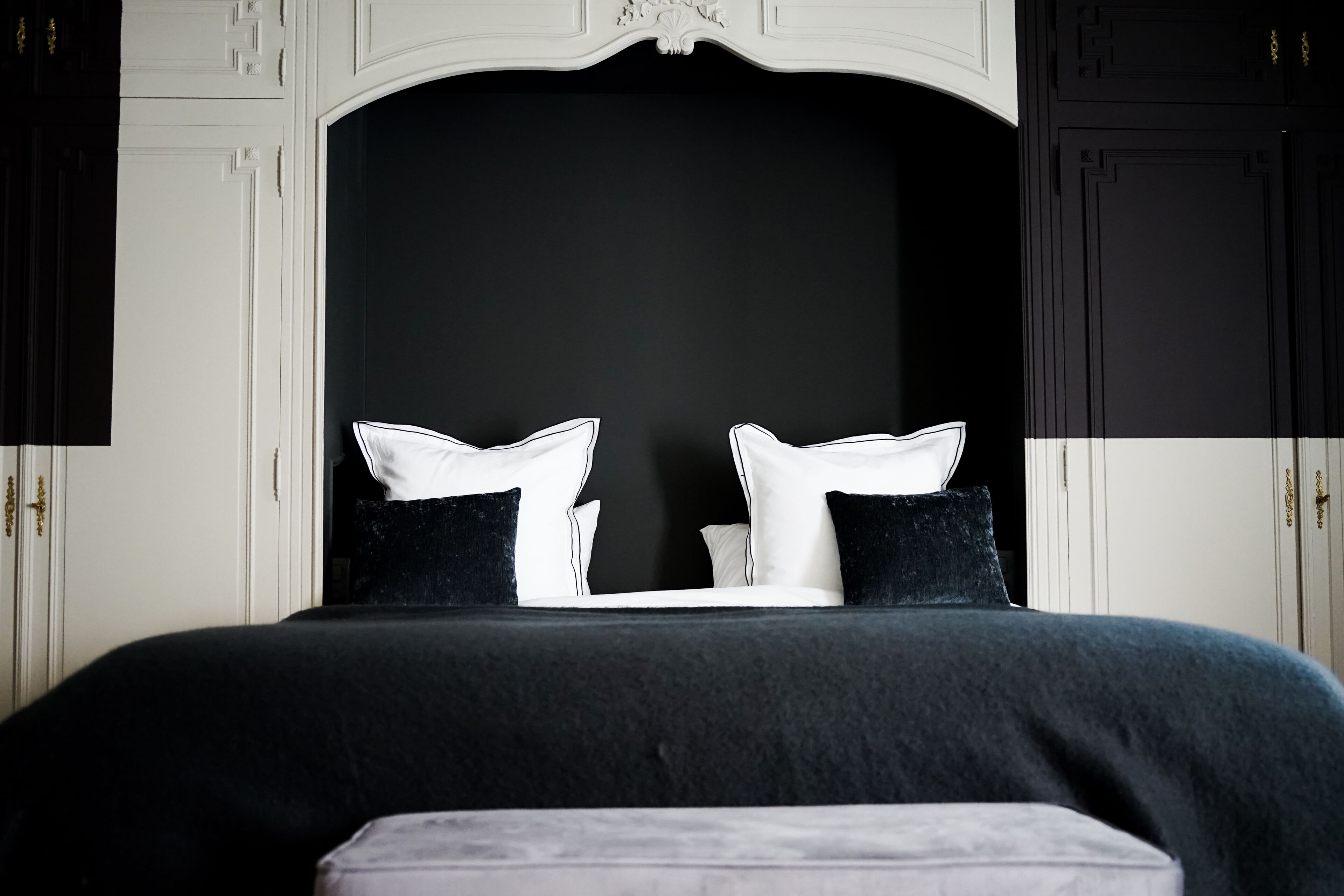 Una cama con ropa de cama blanca y negra, un cabecero oscuro y una mesita de noche blanca.