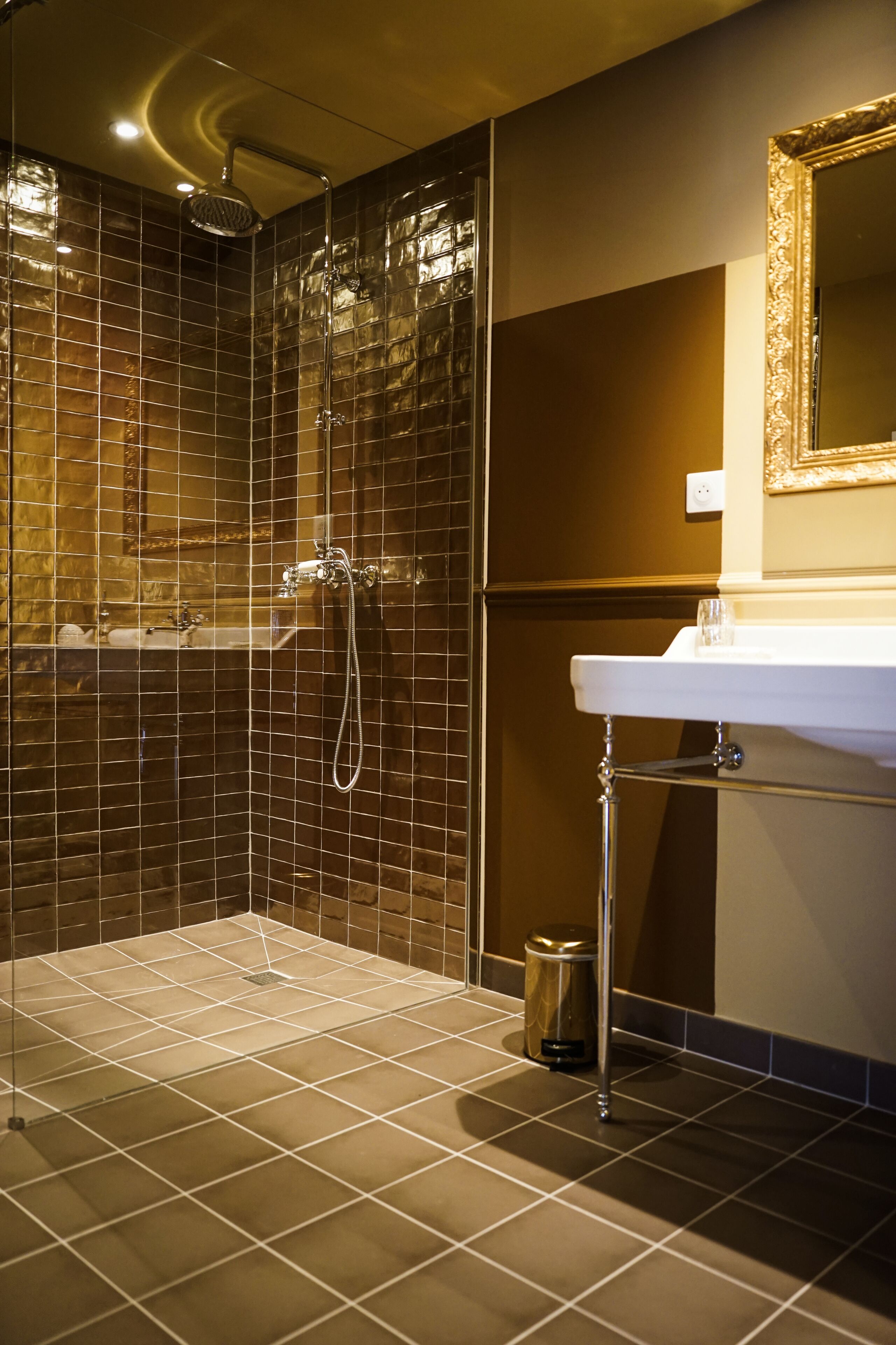 Un baño moderno con ducha envuelta en vidrio, lavamanos blanco y espejo con marco decorativo.