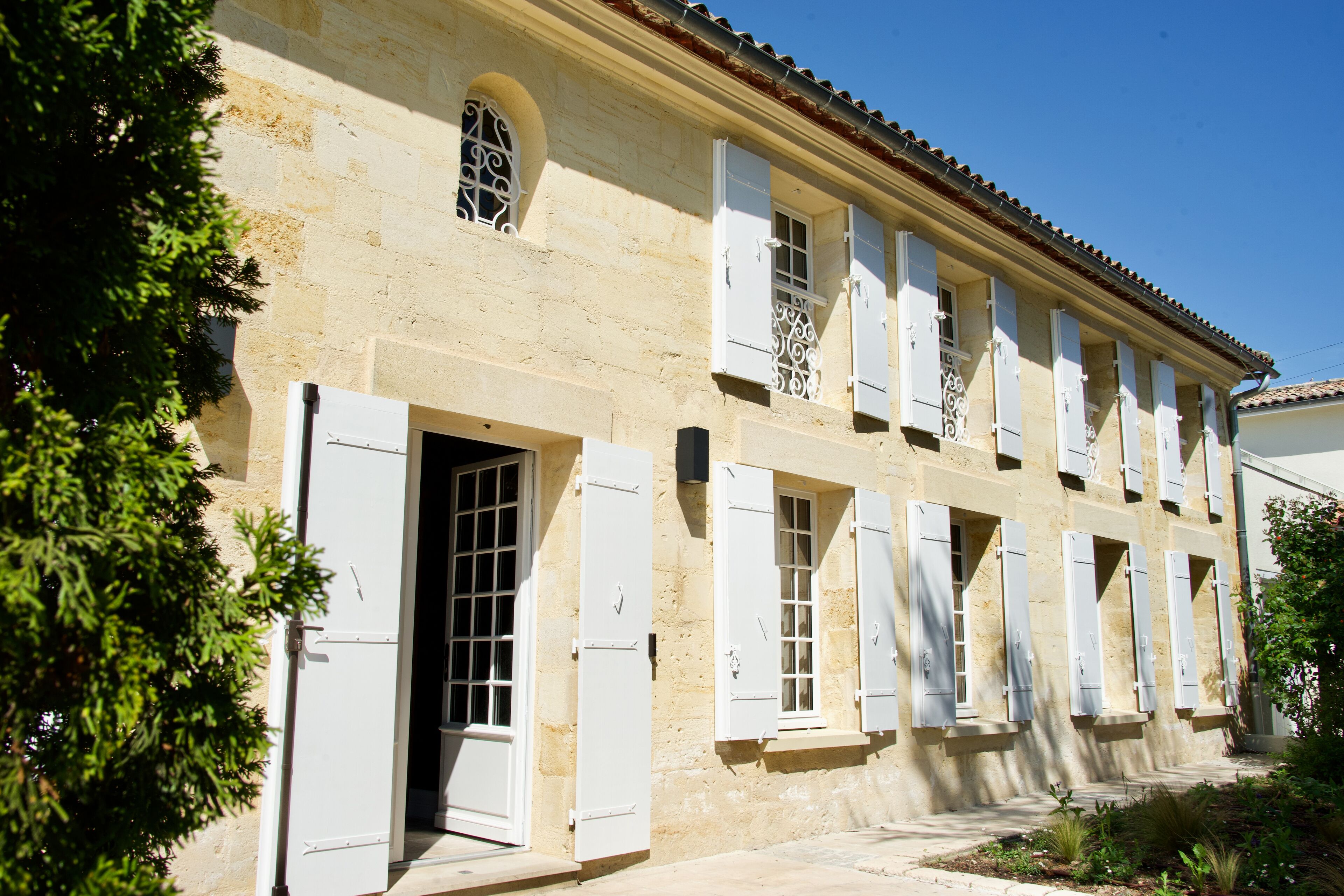 A historic building with multiple windows and doors, featuring a traditional architectural style with white shutters and a tiled roof.