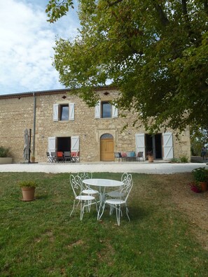 Un bâtiment en pierre doté d’un patio comprenant une table ronde et des chaises.