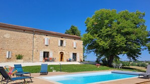 Un bâtiment en pierre doté d’une piscine, d’un espace extérieur aménagé et d’un grand arbre.