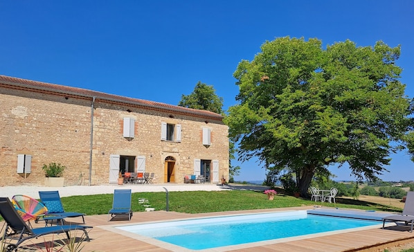 Un bâtiment en pierre doté d’une piscine, d’un espace extérieur aménagé et d’un grand arbre.